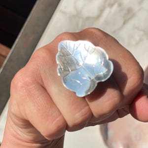 Op de afbeelding: Een zilveren ring in de vorm van een blad met gedetailleerde nerven. De ring wordt aan een vinger gedragen.