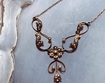 May include: A gold necklace with a delicate floral design and pearl accents. The necklace has a chain link style and a pendant with a flower shape.