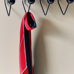 May include: A red and black patterned scarf hanging on a black metal coat rack with round knobs.