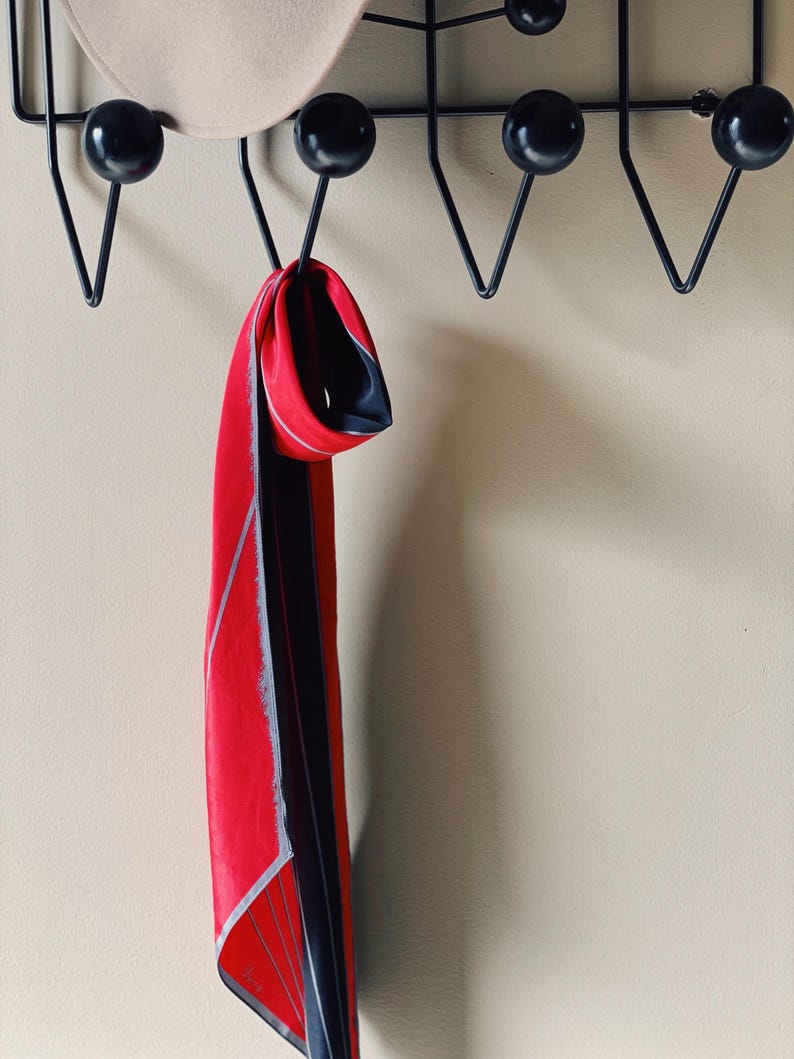 May include: A red and black patterned scarf hanging on a black metal coat rack with round knobs.