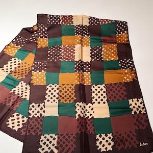 Könnte beinhalten: Ein brauner, grüner und beigefarbener Seidenschal mit Patchwork-Design. Der Schal hat ein sich wiederholendes Muster aus Quadraten in verschiedenen Farbtönen mit einem strukturierten, gepunkteten Overlay. Der Markenname "Echo" ist auf der Ecke aufgedruckt.