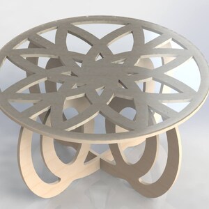 May include: A round wooden coffee table with a decorative, openwork design on the tabletop. The tabletop is a light gray color, and the base is made of curved, natural wood pieces. The table is approximately 24 inches in diameter.