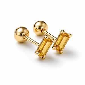 May include: A pair of gold stud earrings featuring a polished spherical back and a rectangular baguette-cut yellow gemstone set in a four-prong gold setting. The earrings have a straight post and a smooth, reflective metallic finish throughout.