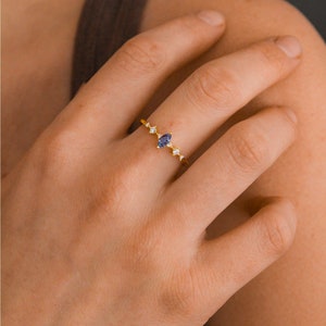 May include: A gold ring with a marquise-shaped blue gemstone and smaller clear gemstones on the band.