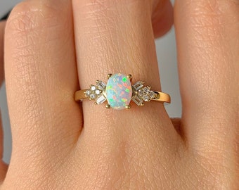 May include: A gold ring with an oval-shaped opal gemstone surrounded by smaller clear gemstones.