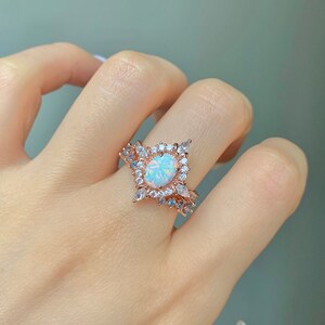 May include: A rose gold ring with a large oval opal gemstone surrounded by smaller clear and blue gemstones.