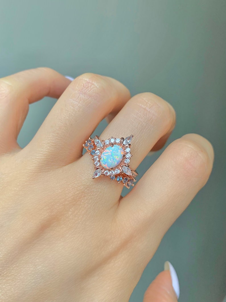 May include: A rose gold ring with a large oval opal gemstone surrounded by smaller clear and blue gemstones.