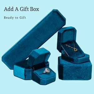 May include: Three teal blue velvet gift boxes, one is a long rectangular box, one is a square box, and the other is a heart-shaped box. The square box is open and contains a gold necklace with a green gemstone pendant. The heart-shaped box is closed. The long rectangular box is closed. Add A Gift Box, Ready to Gift.