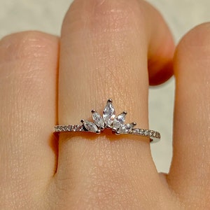 May include: A silver ring with a crown of small, clear cubic zirconia stones. The ring is on a finger.
