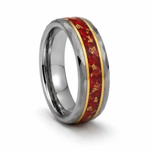 May include: A faceted silver-toned ring featuring a central inlay of deep red material speckled with gold-colored flakes, bordered by thin gold-toned bands. The exterior surface of the ring has a geometric, multi-faceted texture throughout.