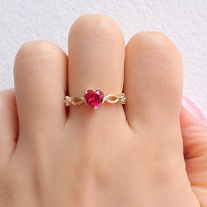 May include: A gold ring with a red heart-shaped gemstone and small clear gemstones on the band.