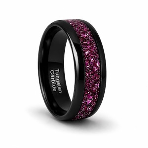 May include: A black tungsten carbide ring with a vibrant magenta inlay. The ring has a polished finish and features the text "Tungsten Carbide" on the side. The magenta inlay is made of small, sparkling fragments.