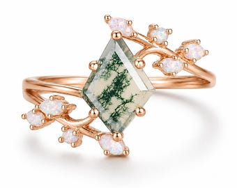 Op de afbeelding: Een roségouden ring met een centrale vliegervormige mosagaat edelsteen met donkergroene insluitingen. De ringband is versierd met kleine, marquise-geslepen iriserende opalen die in een takachtig patroon vanaf de centrale steen uitlopen.