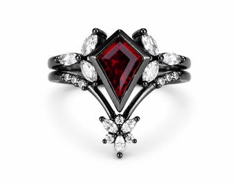 May include: A black metal ring set featuring a central kite-shaped red gemstone. The band is accented with multiple marquise-cut and round-cut white stones arranged in a leaf-like pattern surrounding the primary red stone in a layered design.