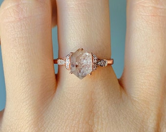 May include: A rose gold ring with a clear hexagonal gemstone surrounded by smaller clear gemstones.