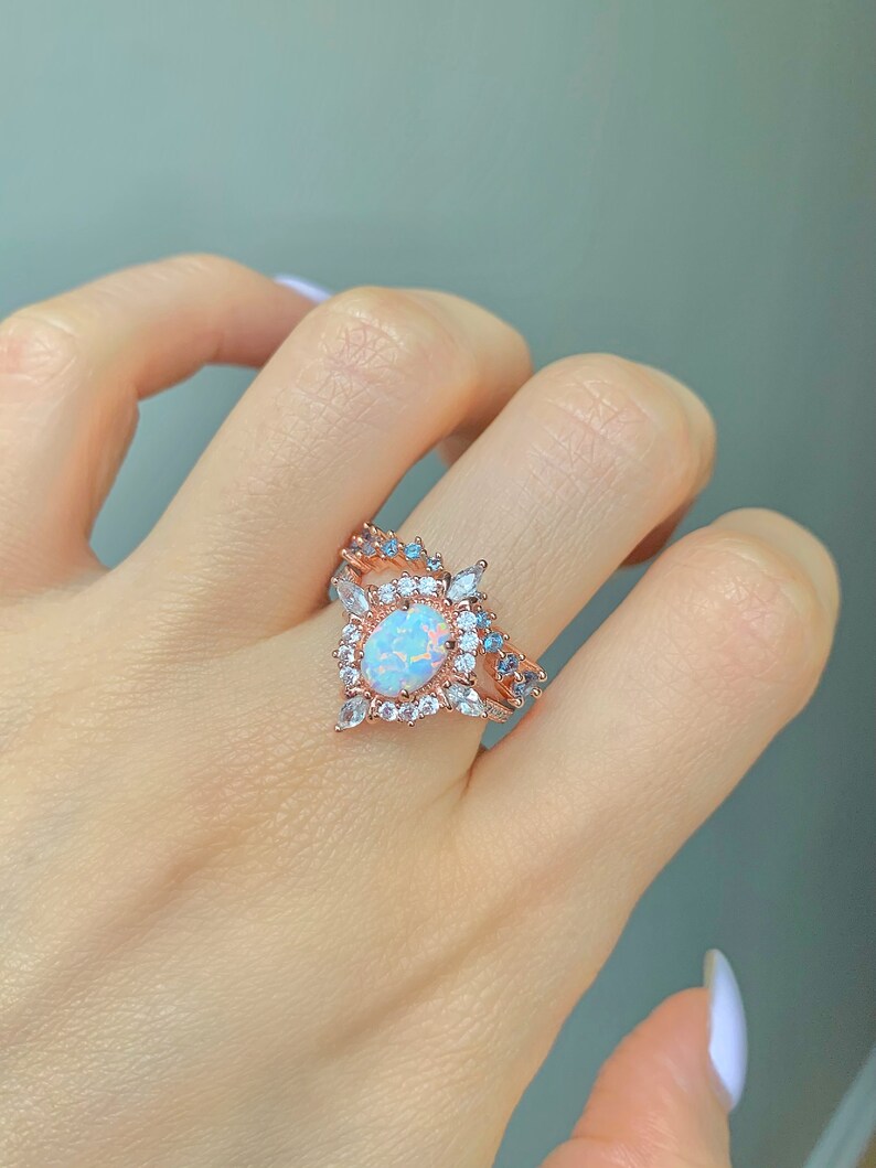 May include: A rose gold ring with a large oval opal surrounded by smaller clear and blue stones.