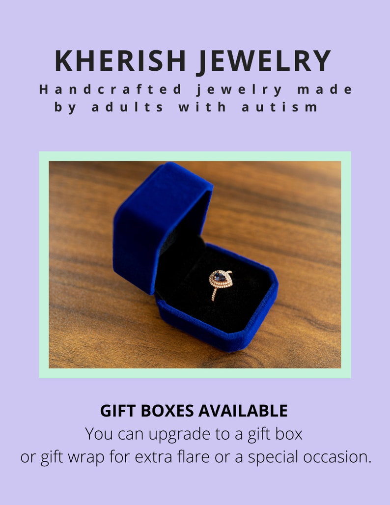 May include: A blue velvet ring box with a gold ring with a purple gemstone inside. The box is sitting on a wooden surface.  "KHERISH JEWELRY Handcrafted jewelry made by adults with autism GIFT BOXES AVAILABLE You can upgrade to a gift box or gift wrap for extra flare or a special occasion."
