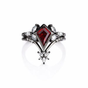 May include: A black engagement ring set featuring a red, diamond-shaped central stone. The ring is adorned with white gemstones and a floral motif at the base. Includes a matching band.