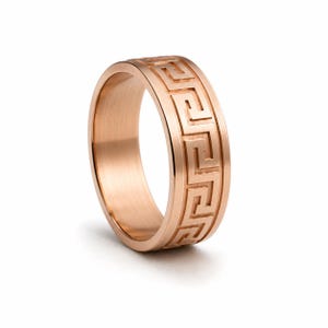May include: Rose gold ring with a Greek key pattern. The ring has a flat band and a continuous geometric design around the exterior. The ring is made of a shiny, metallic material.