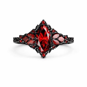 May include: A black ring with a central marquise-cut red gemstone, surrounded by smaller red stones and intricate black metalwork. The ring has a gothic or vintage aesthetic, with a detailed band.