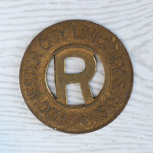 May include: A gold-colored metal token with the words "Rochester City Lines" and the letter "R" in the center.