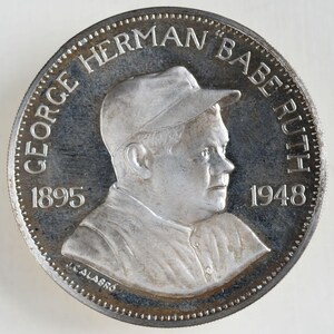 May include: A silver coin with a profile image of George Herman "Babe" Ruth, a famous baseball player. The coin has the years 1895 and 1948 inscribed on it.