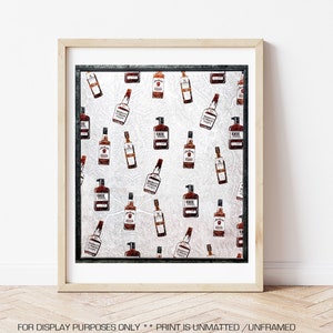 May include: A framed print featuring a repeating pattern of whiskey bottles in various styles and brands. The bottles are brown and amber, set against a textured, silver-toned background. The frame is light wood with a black border. Text at the bottom reads: FOR DISPLAY PURPOSES ONLY ** PRINT IS UNMATTED / UNFRAMED