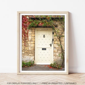 May include: A vintage-style, cream-coloured door with a black door knocker and a small mailbox. The door is surrounded by a stone wall covered in ivy with red leaves.