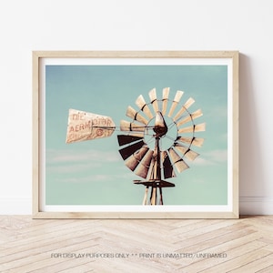 May include: A vintage windmill with a weathered wooden frame and rusted metal blades against a blue sky. The windmill has a sign that reads "The Aermotor Co. Chicago".