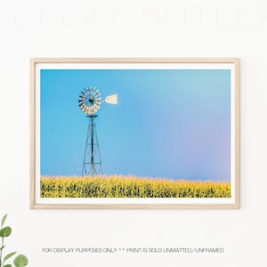 May include: A framed photograph of a windmill in a field of yellow grass against a blue sky. The windmill has a white blade and is silhouetted against the sky.