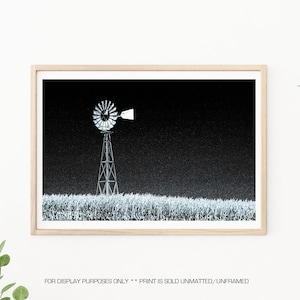 May include: A black and white photograph of a windmill in a field. The windmill is silhouetted against a dark sky.