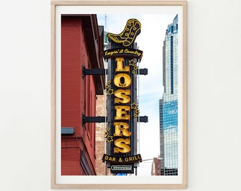 Puede incluir: Un letrero de neón para un bar y parrilla llamado "Losers" con un gráfico de bota de vaquero y el texto "Keepin' it Country". El letrero está frente a un edificio de ladrillo rojo en un entorno urbano.