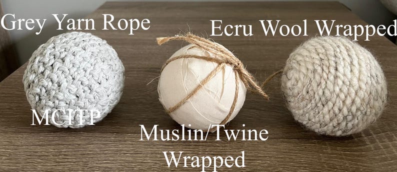 K&ouml;nnte beinhalten: Drei runde Ornamente, die in verschiedenen Materialien verpackt sind. Das erste ist in graues Garnseil verpackt, das zweite in Musselin und Schnur und das dritte in ecrufarbener Wolle. Der Text "Grey Yarn Rope", "Muslin/Twine Wrapped" und "Ecru Wool Wrapped" ist &uuml;ber jedem Ornament sichtbar.