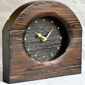 Puede incluir: Un reloj de madera marrón oscuro con una esfera redonda y agujas doradas. El reloj tiene forma de arco y tiene un aspecto rústico.