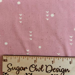 May include: Pink fabric with a repeating pattern of white triangles and starburst shapes. A wooden ruler with the text "Sugar Owl Design" is placed across the fabric, measuring in inches.