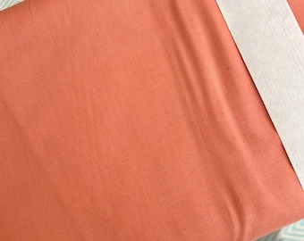 May include: A close-up of a terracotta-colored fabric with a subtle linen texture. The fabric is folded and has a white tape along the edge.