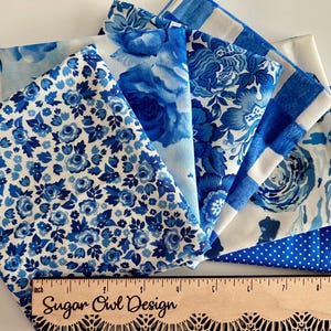 May include: A collection of blue and white fabric swatches with various floral, polka dot, and checkered patterns. A wooden ruler with the text "Sugar Owl Design" is at the bottom, measuring in inches.