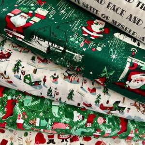 May include: A stack of Christmas-themed fabric rolls. The fabrics feature festive designs including Santa Claus, Christmas trees, stockings, and reindeer. Colors include green, red, white, and brown. Some fabric has text printed on it.