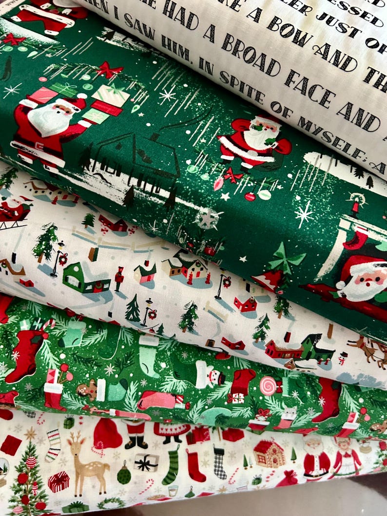 May include: A stack of Christmas-themed fabric rolls. The fabrics feature festive designs including Santa Claus, Christmas trees, stockings, and reindeer. Colors include green, red, white, and brown. Some fabric has text printed on it.