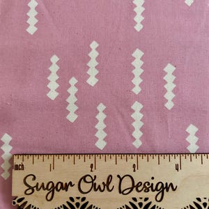 May include: Pink fabric with a repeating pattern of white zig-zag shapes. A wooden ruler with the text "Sugar Owl Design" is placed on the fabric, measuring up to 4 inches.