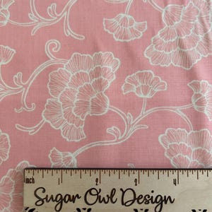 May include: Pink fabric with a white floral pattern. The fabric features large, stylized flowers and flowing vines. A wooden ruler with the text "Sugar Owl Design" is placed on the fabric, measuring in inches.