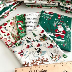 May include: Assorted Christmas-themed fabric bundles featuring festive patterns. Designs include Santa Claus, reindeer, Christmas trees, and holiday text. The fabrics are in shades of green, red, white, and beige. A wooden ruler with the text "Sugar Owl Design" is also visible.