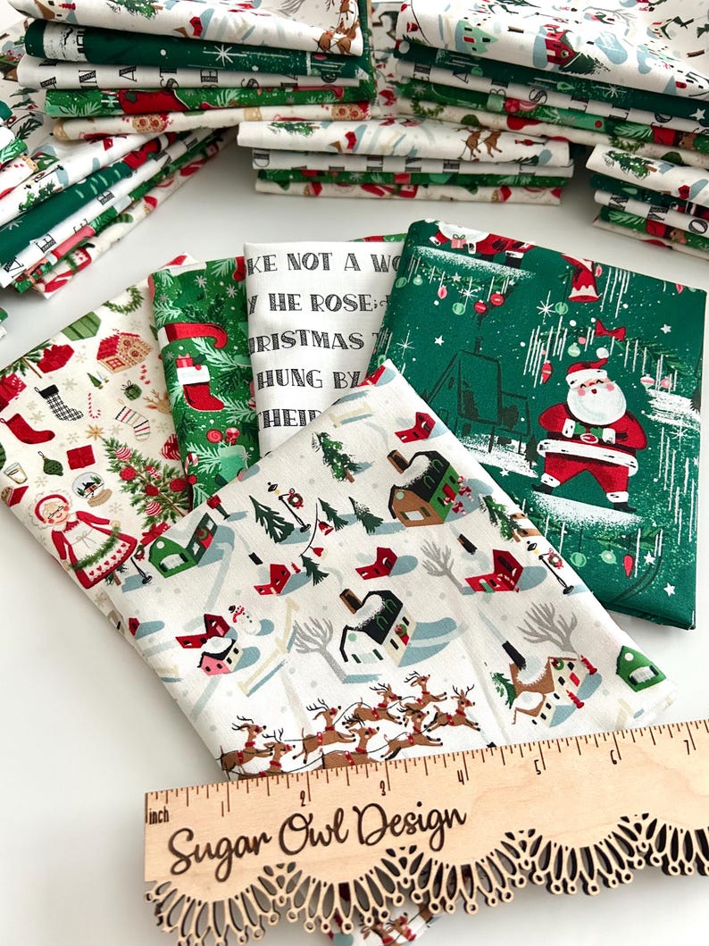 May include: Assorted Christmas-themed fabric bundles featuring festive patterns. Designs include Santa Claus, reindeer, Christmas trees, and holiday text. The fabrics are in shades of green, red, white, and beige. A wooden ruler with the text "Sugar Owl Design" is also visible.