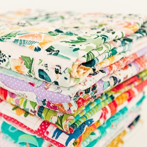 May include: A stack of colourful fabric squares with floral, geometric and animal prints. The fabric squares are folded and stacked on top of each other.