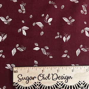 May include: Burgundy fabric with a white leaf and dot pattern. A wooden ruler with the text "Sugar Owl Design" is placed on the fabric. The ruler measures up to 5 inches.