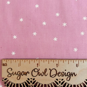May include: Pink fabric with a repeating pattern of white snowflakes. A wooden ruler with the text "Sugar Owl Design" is placed on the fabric. The ruler measures up to 4 inches.