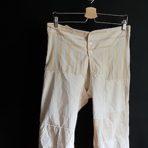 Può includere: Pantaloni bianchi in cotone con strisce gialle e dettagli a toppe. I pantaloni hanno una chiusura a bottone e una vestibilità larga a gamba larga.