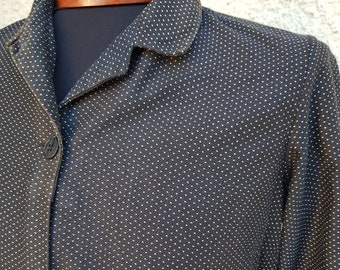 May include: A black long-sleeved shirt with a white polka dot pattern. The shirt has a collar and a button-up front. The shirt is belted at the waist.