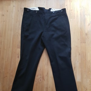 Puede incluir: Pantalón negro con cierre de botón y forro a cuadros blanco y negro en la cintura.
