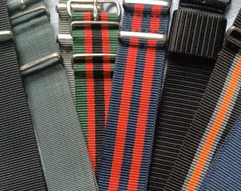 May include: A collection of nylon watch straps featuring various designs, including solid black, solid gray, and striped patterns in red and black, blue and red, black and orange, and solid blue, all equipped with silver-toned metal buckles and loops.